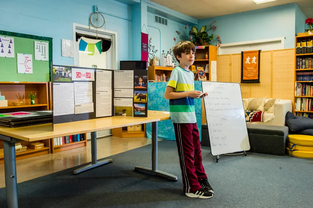 A student stands at the front of the class in front of an exhibit of their work.