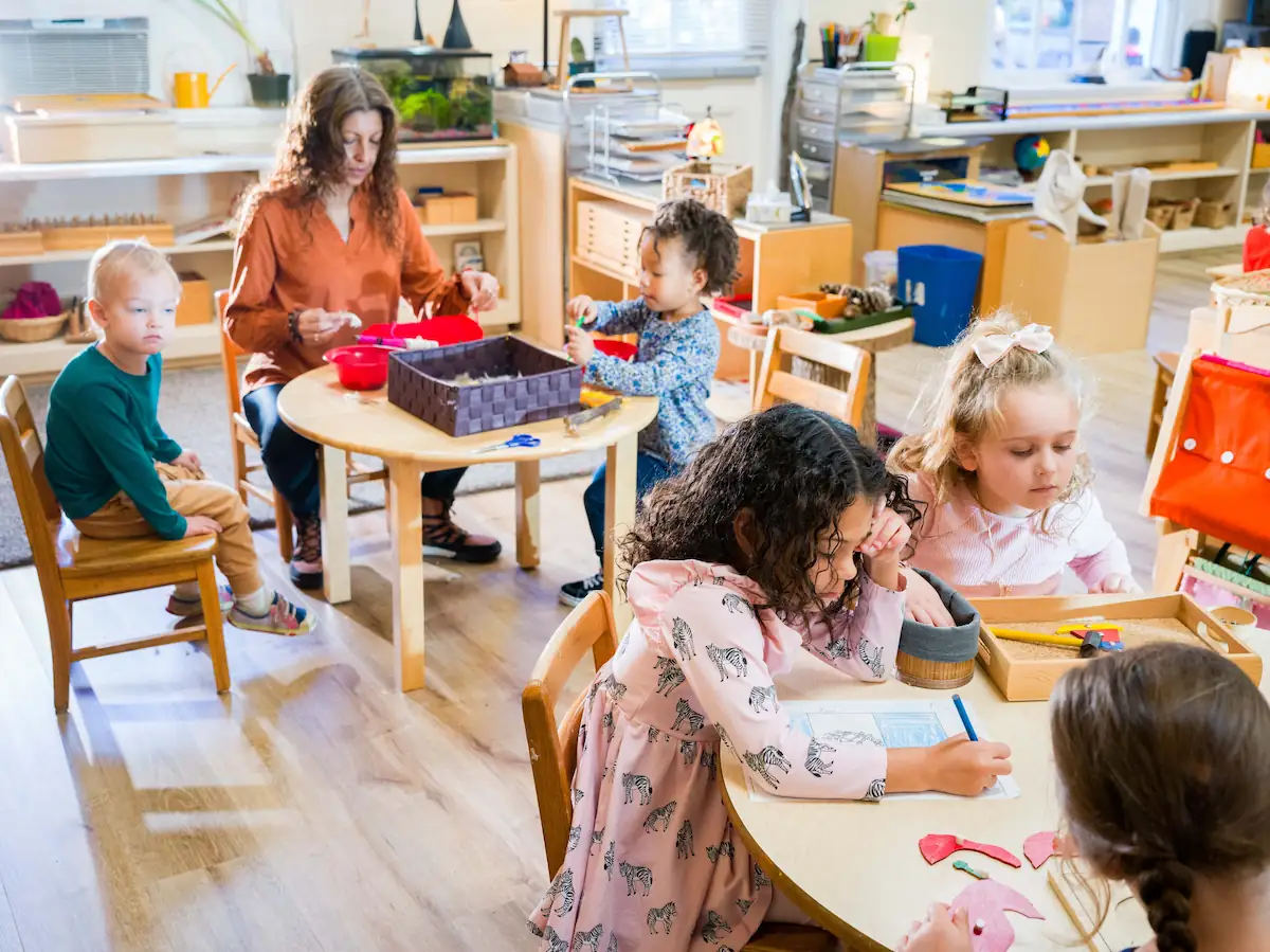 A bright and sunny classroom scene with two round desks and students working on different projects.