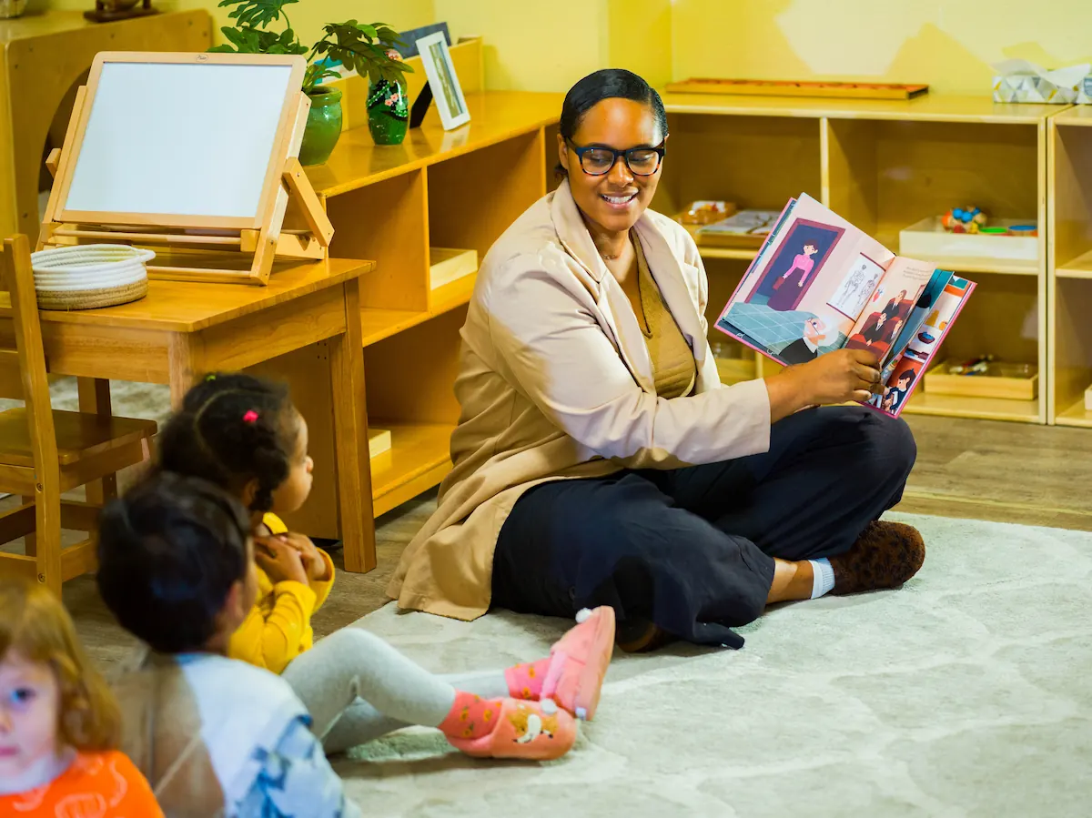 A teacher is reading from a story book to a group of young children