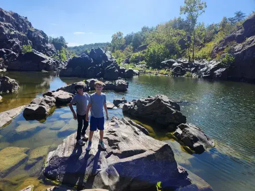 Two students are standing on a rock in front of a river.