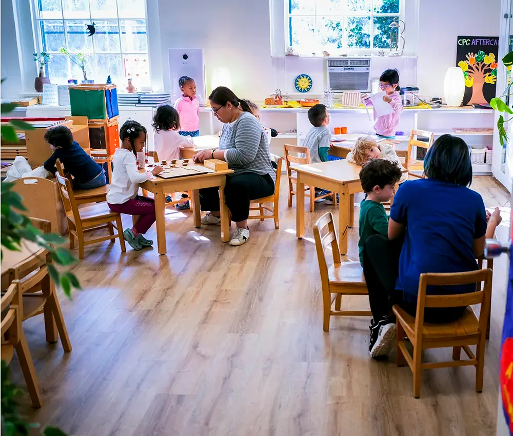 A busy classroom scene with students working on different things while teachers are going round assisting.