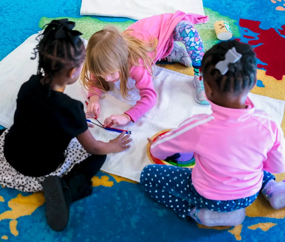Three young students are sat on the carpet working on a craft project.