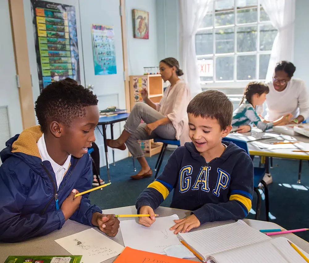 Two young students are sat together comparing drawings.