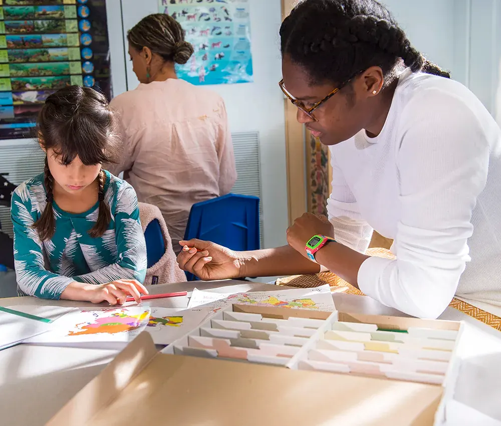 A teacher is sat assisting a student with her geography work.