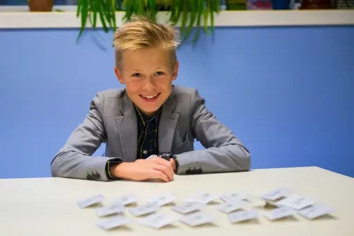 A smiling student in a grey blazer sits at a desk