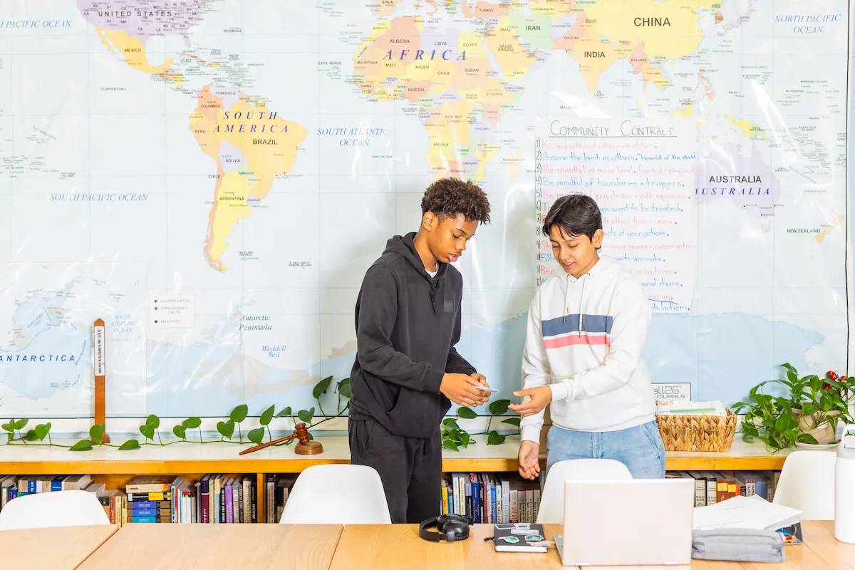 Two students are in front of a world map.