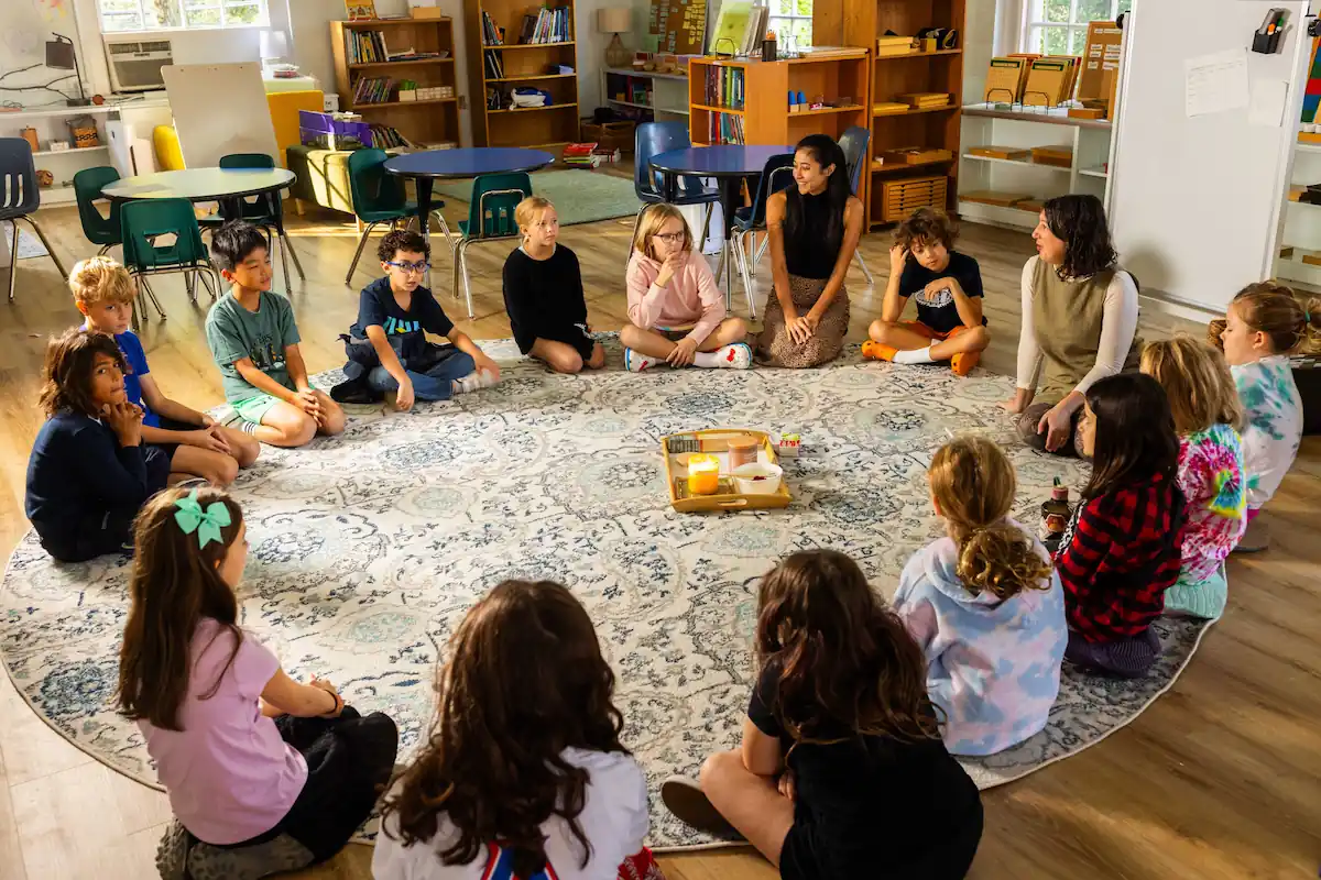 A group of children are sat in a circle around a large round rug