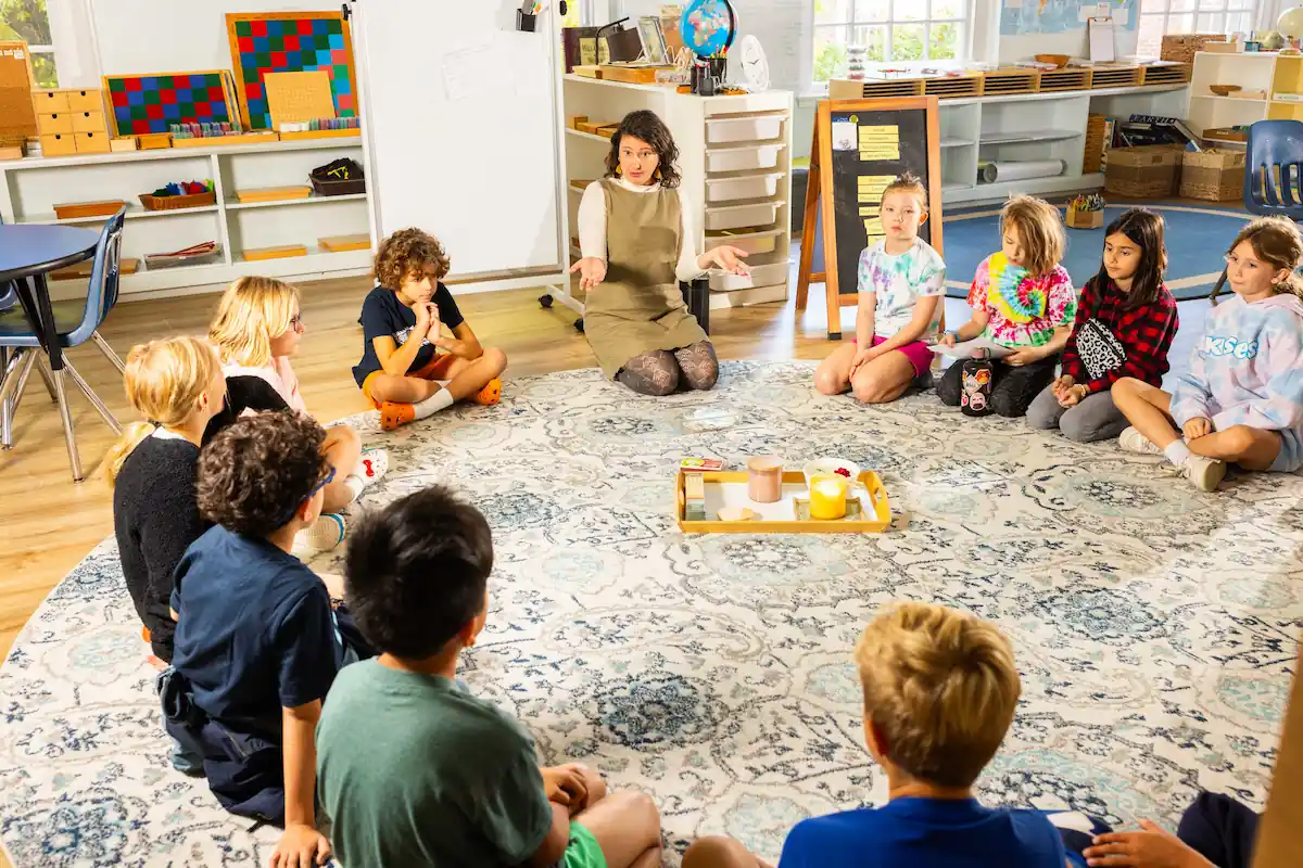 A group of children sit in a circle participating in a discussion with a teacher