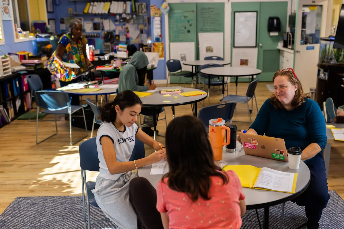 Students are sat at a round desk working on their projects.