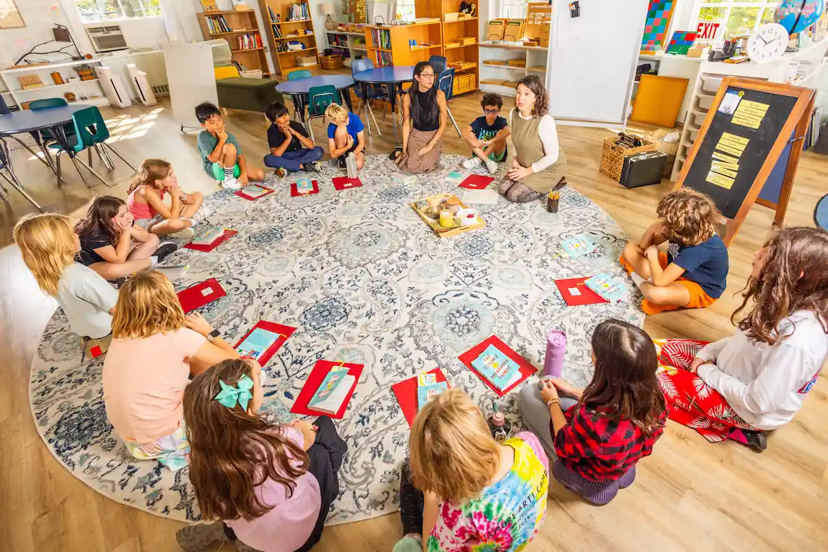 Students sit in a circle on the floor listening to the teacher speak