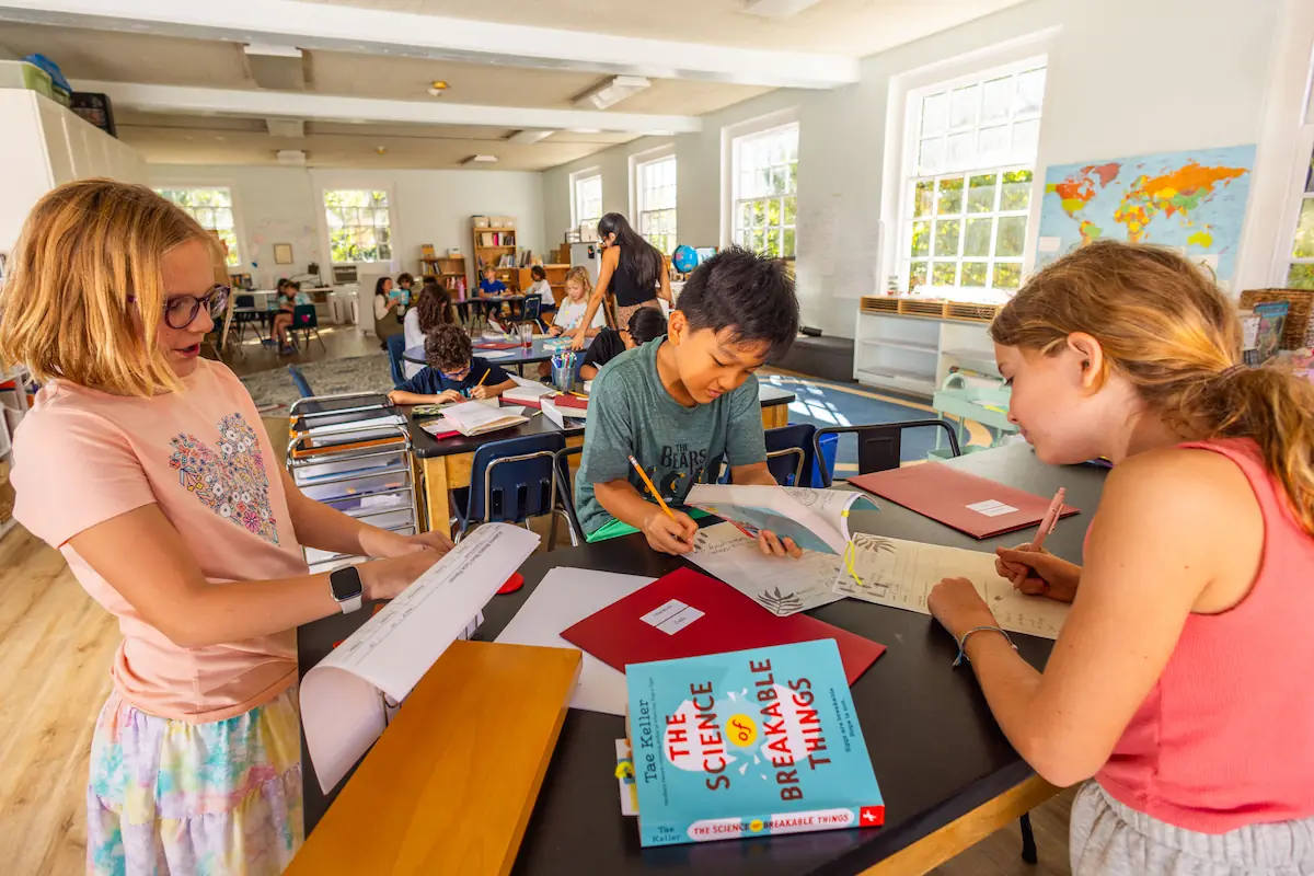 Three students in the foreground are writing and referring to their science books