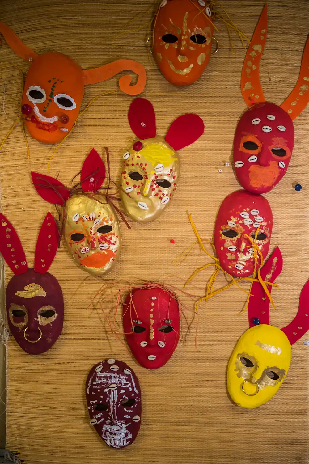A number of colourful masks with animal ears are laid out over a braided textured background.