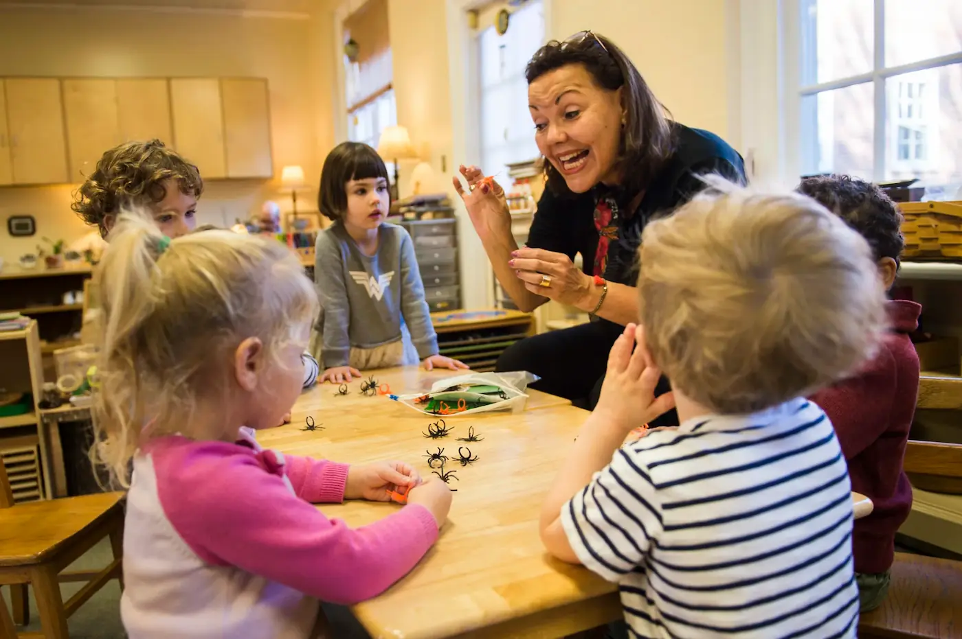 A teacher is leading a language session at a small desk with five young students.