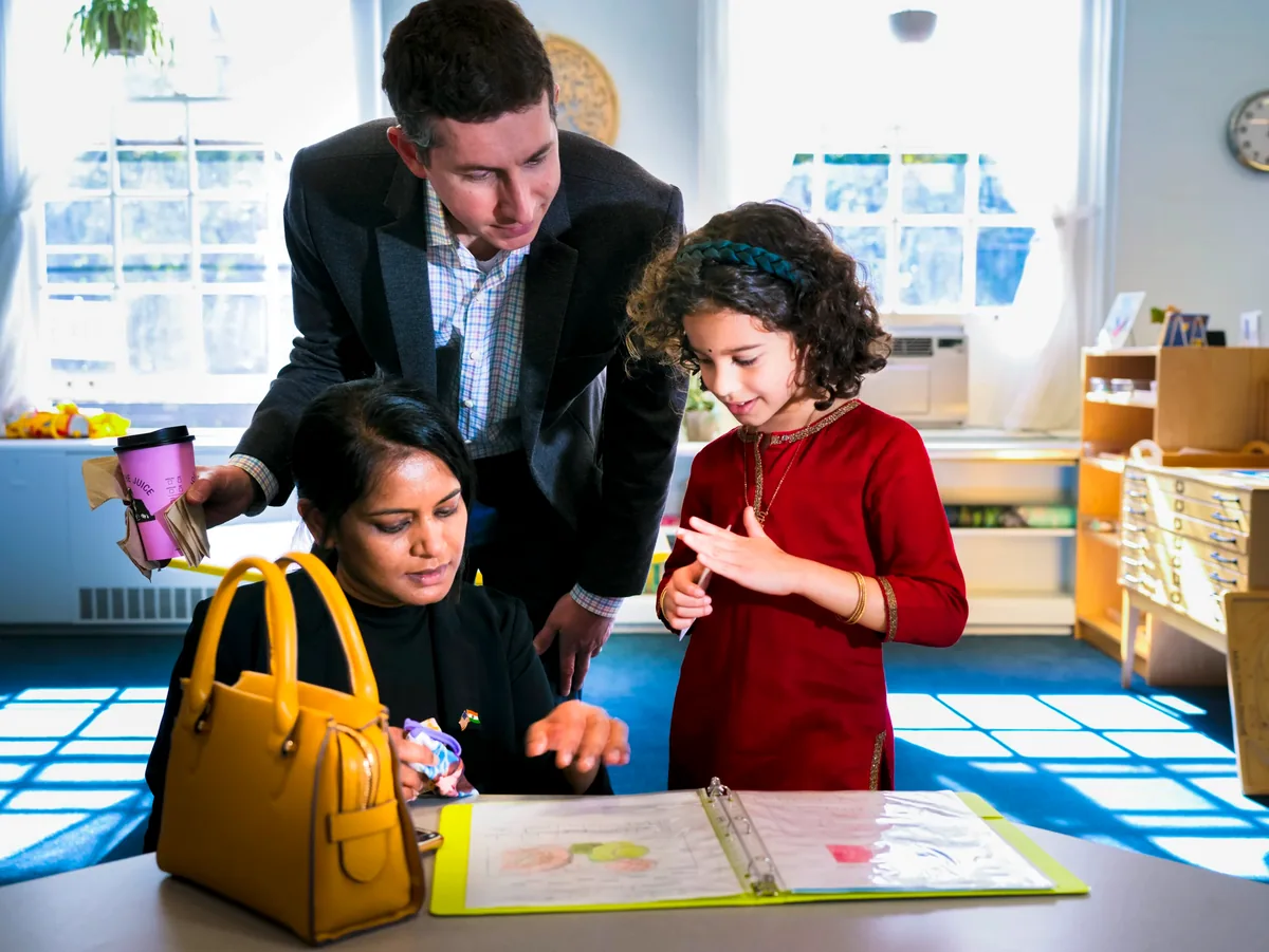 Two adults are carefully looking over a young student's work presented in a folder.