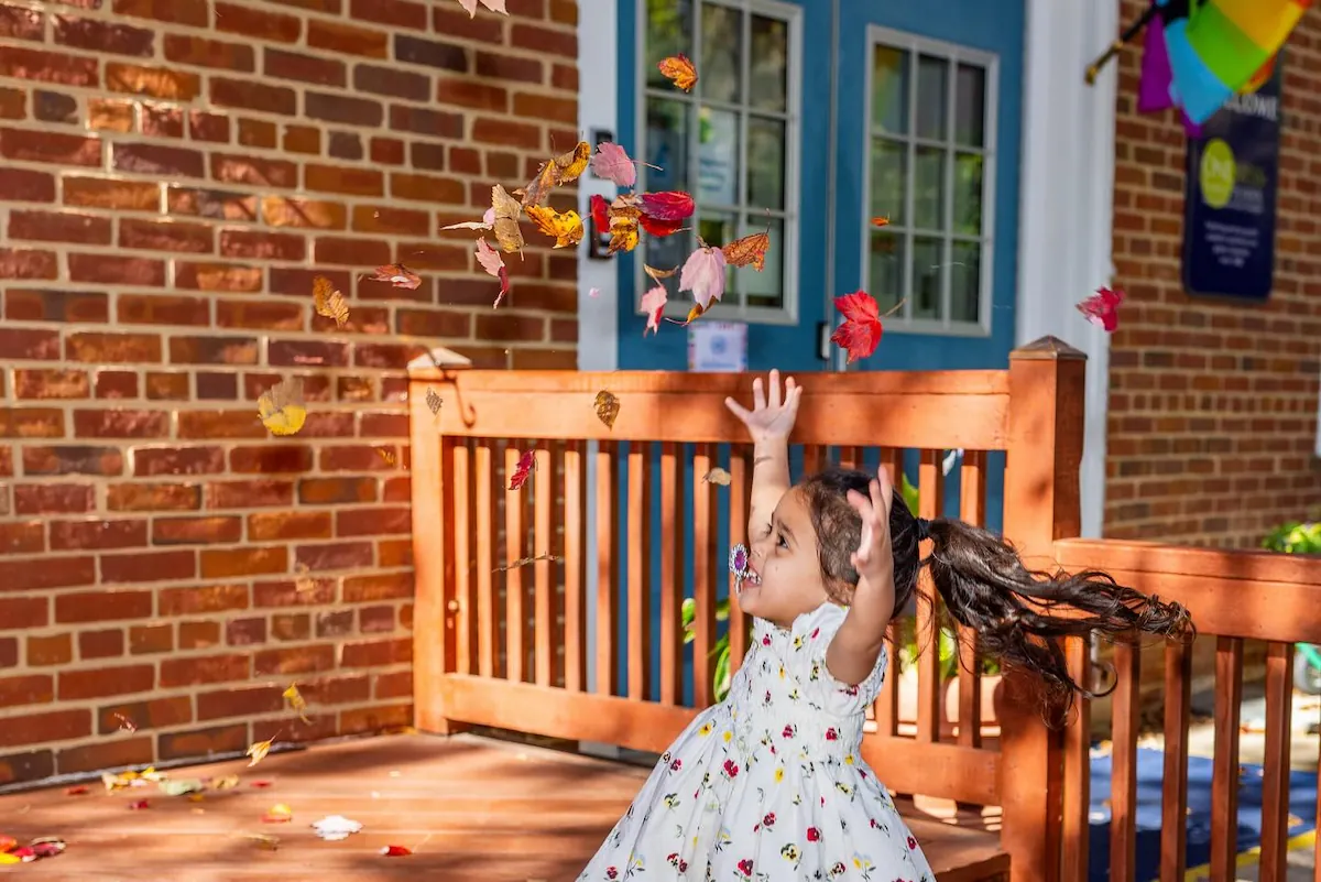 A young girl is playing with autumn leaves outside.